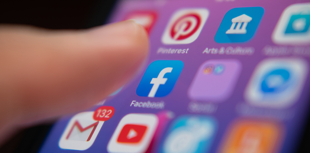 A smartphone screen displaying app icons including Facebook, YouTube, and Pinterest. A finger hovers over Facebook, suggesting engagement or selection.